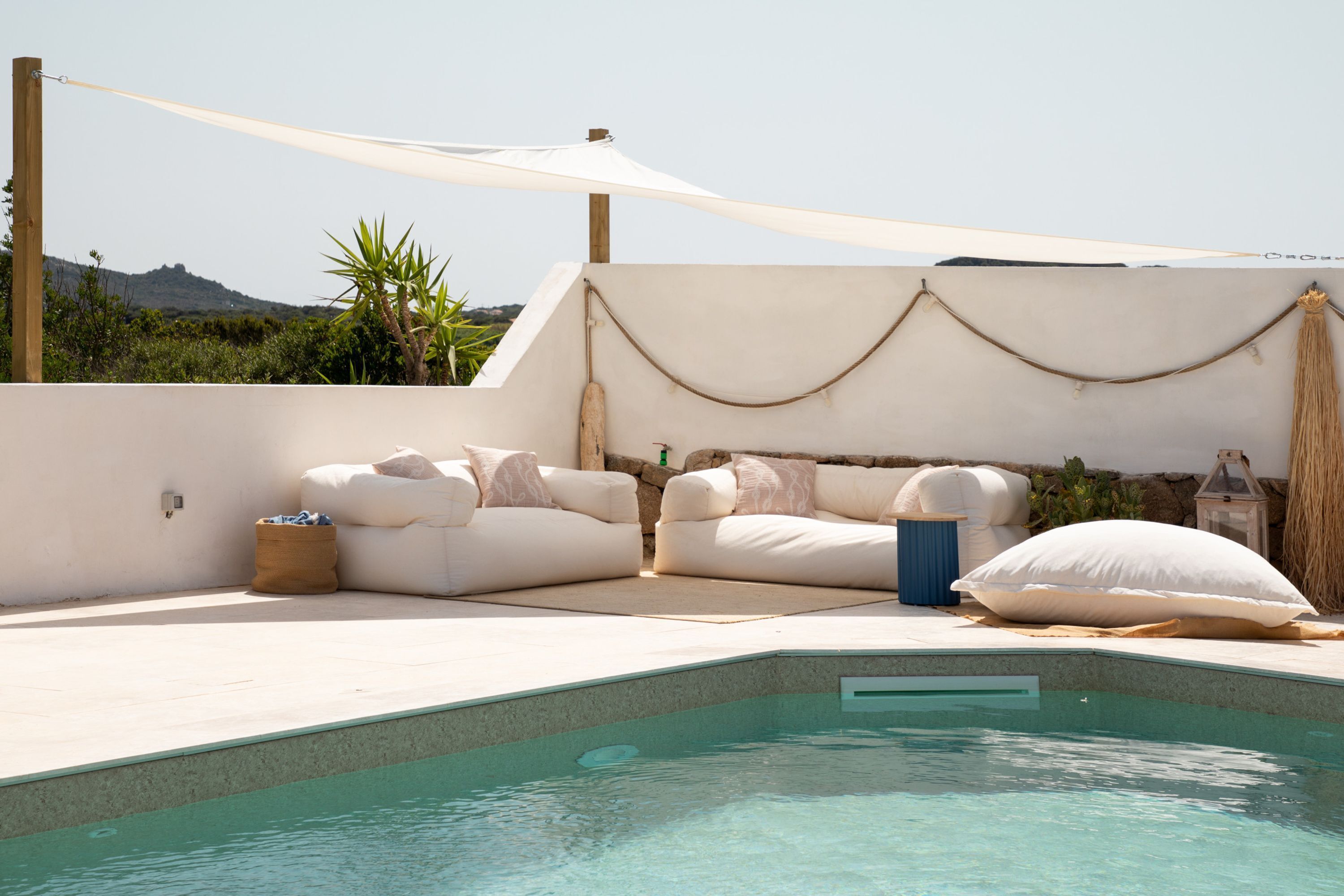 Zona de piscina con un conjunto de sofá blanco para exteriores, un pequeño bote de basura y un farol decorativo.