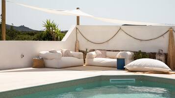 Zona de piscina con un conjunto de sofá blanco para exteriores, un pequeño bote de basura y un farol decorativo.