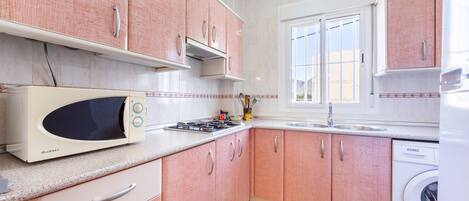 Une cuisine avec des meubles de couleur rose, un four à micro-ondes, une cuisinière, un évier et un lave-linge.
