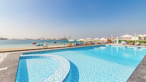 A swimming pool with a view of the sea and beach umbrellas. - GLOBALSTAY. Azizi Royal Bay Apartments (Dubai)
