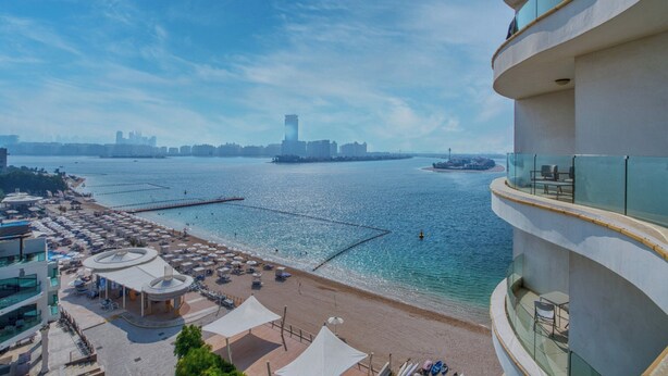 A coastal hotel with a beach view, a pool area, and a city skyline in the background. - GLOBALSTAY. Azizi Royal Bay Apartments (Dubai)