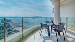 A balcony with a table and chairs, overlooking a waterfront with buildings in the distance. - GLOBALSTAY. Azizi Royal Bay Apartments (Dubai)