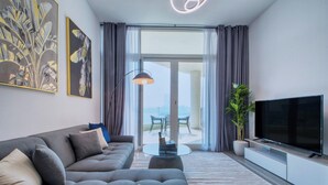 A modern living room with a grey sofa, a flat-screen TV, a coffee table, and a large window with curtains. - GLOBALSTAY. Azizi Royal Bay Apartments (Dubai)