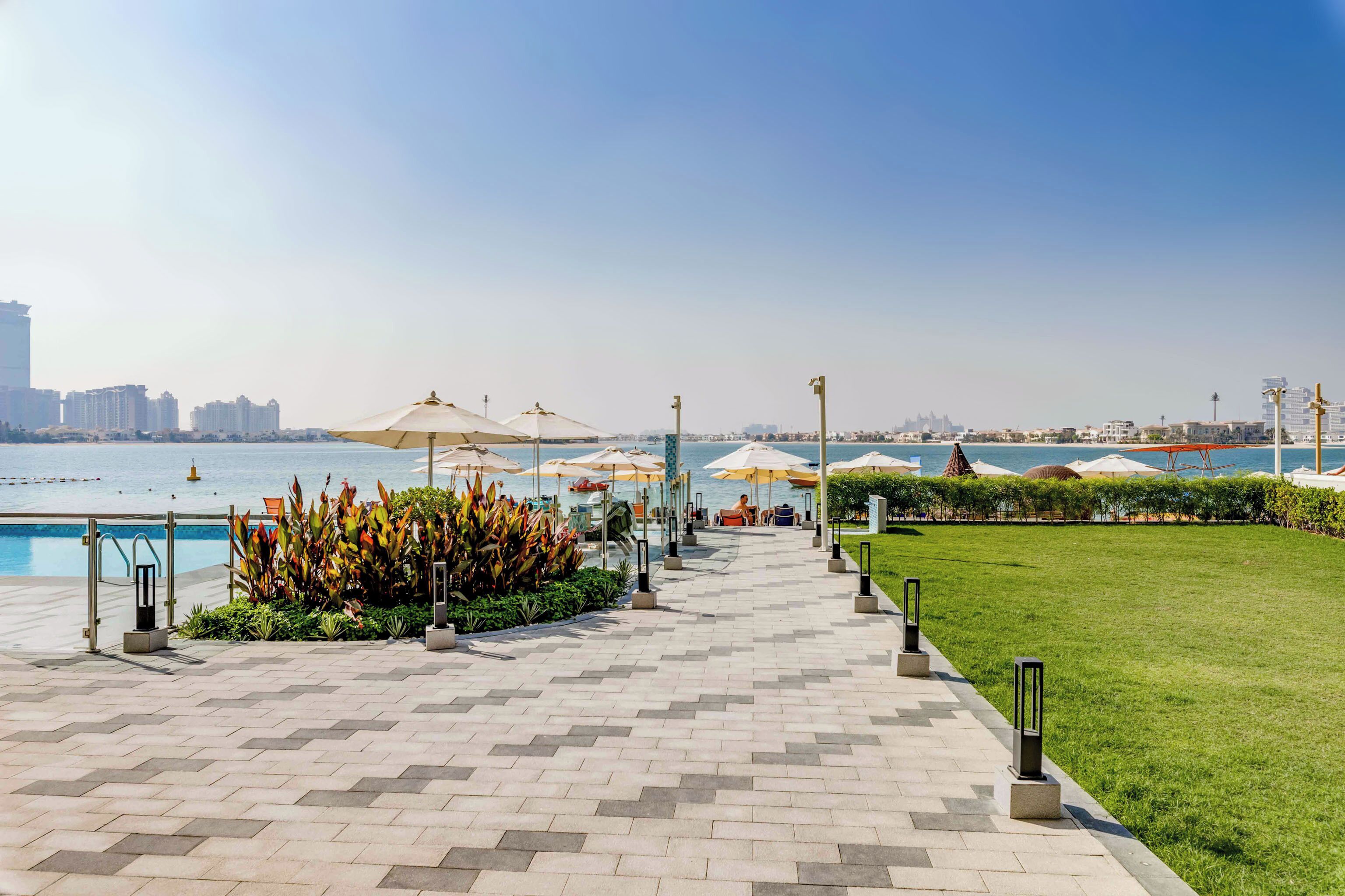 A waterfront promenade with a pool, umbrellas, and a view of the sea.