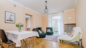 A room with a dining table, two green armchairs, a sofa, a window with curtains, and a ceiling light. - ShortStayPoland Szara B170 (Warsaw)