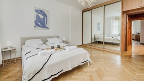A modern bedroom with a large bed, a bedside table, a mirror, and a hanging light fixture. - ShortStayPoland Szara B170 (Warsaw)