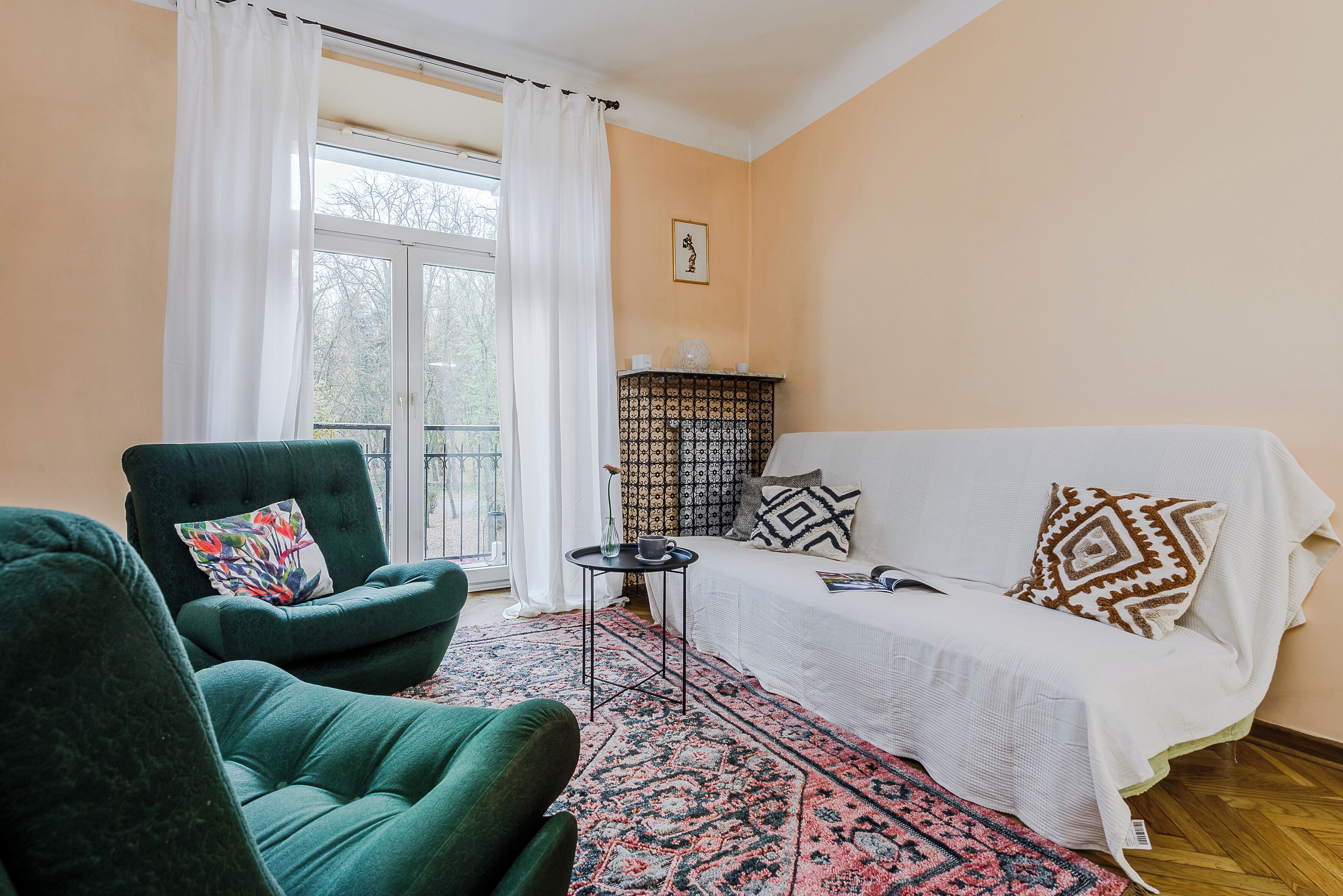 Une pièce avec un fauteuil vert, un canapé blanc, un tapis à motifs et une petite table d’appoint.