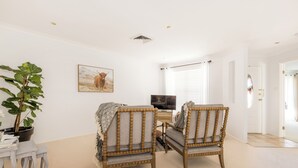 A room with two wooden chairs, a small table, a potted plant, a painting, a television, and a window with blinds. - Room in Studio - Nice Studio on Jasmine (Bomaderry)