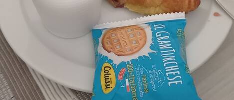 A white cup of coffee, a croissant, and a packet of Colosso biscuits on a white plate.