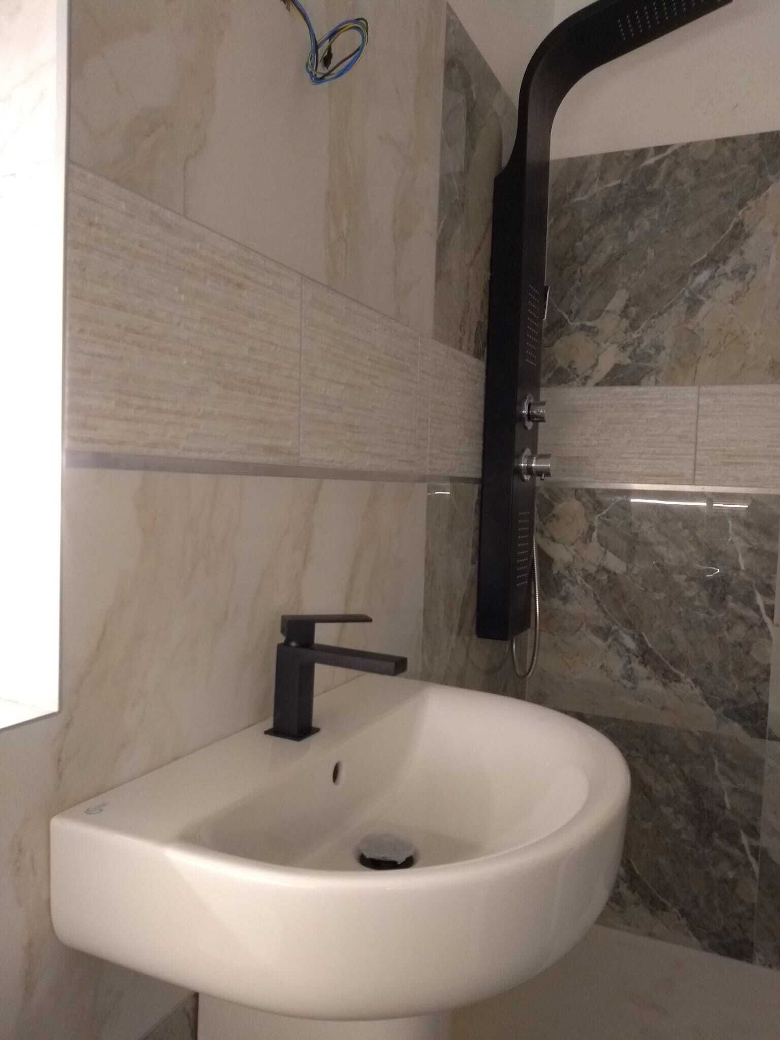 A bathroom with a white sink, a black faucet, and a marble-tiled wall.