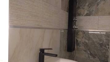 Un baño con un lavamanos blanco, un grifo negro y una pared de azulejos de mármol.