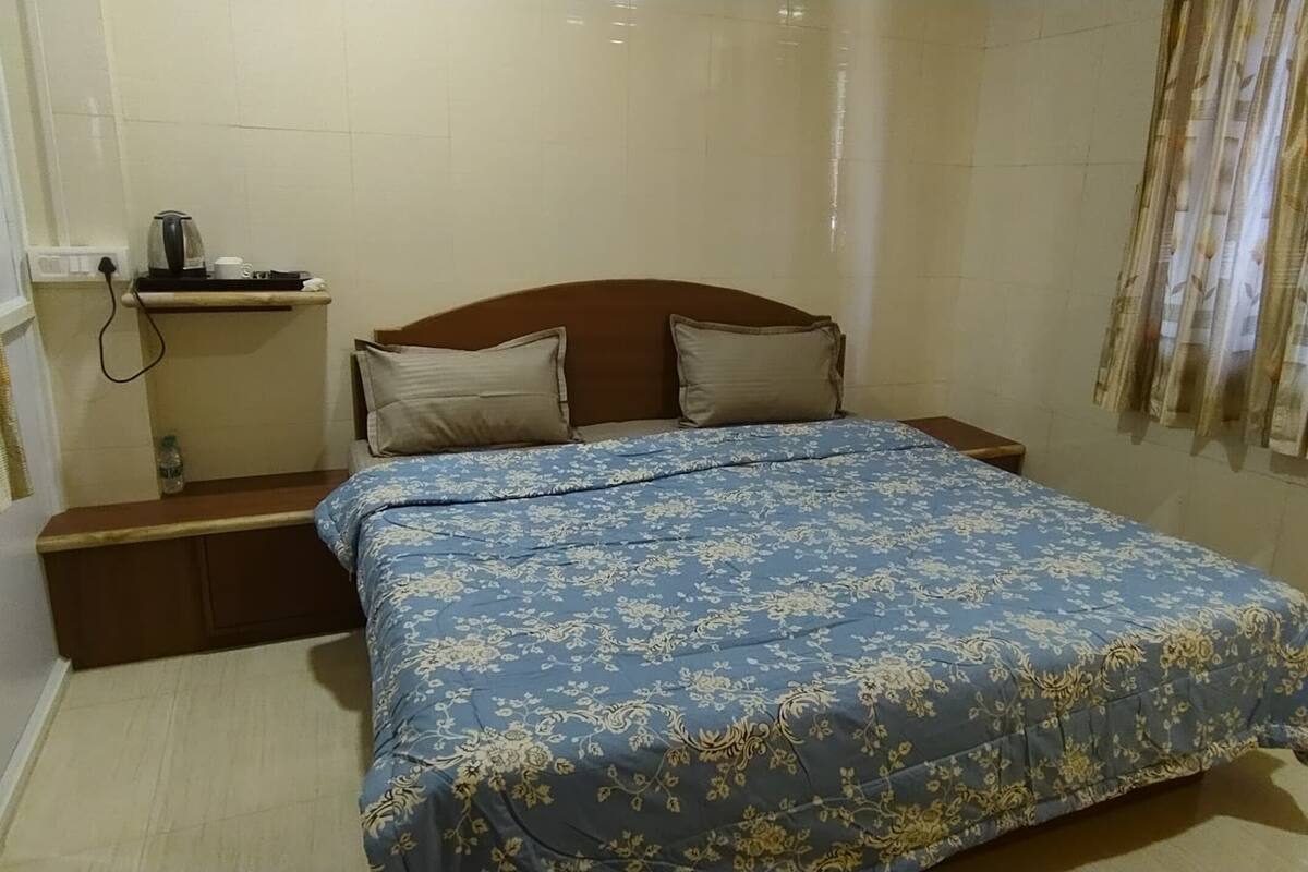 Ein Hotelzimmer mit einem Bett, einem Nachttisch, einem kleinen Tisch mit Wasserkocher und einem Fenster mit Vorhängen.