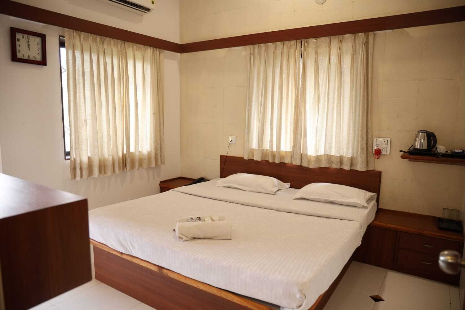 Una habitación de hotel con una cama grande, dos mesitas de noche, un cabecero de madera y un reloj en la pared.