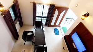 Un comedor con una mesa, sillas, ventilador de techo, televisor y una ventana con cortinas.