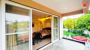 Un dormitorio con cama, una silla y puerta corrediza de vidrio que da a un balcón con vista a zonas verdes.
