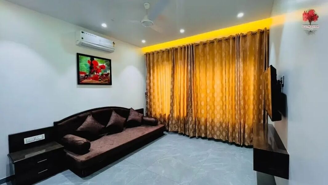 A modern living room with a sofa, a flat-screen TV, and a large window with curtains.
