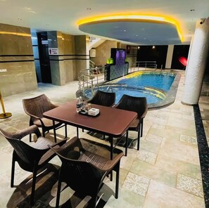 An indoor swimming pool area with a table and chairs, a staircase, and a poolside bar. - Gulmohar Resort And Spa (Mahabaleshwar)
