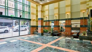 A spacious lobby with a checkered floor pattern, large windows, and a seating area with a bench and potted plants. - Exhibition Street Retreat - Central Stay with Parking (Melbourne)