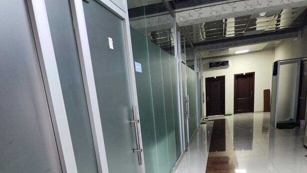 Un couloir doté de portes en verre, d’un sol recouvert de carreaux de marbre et d’une rambarde en métal.