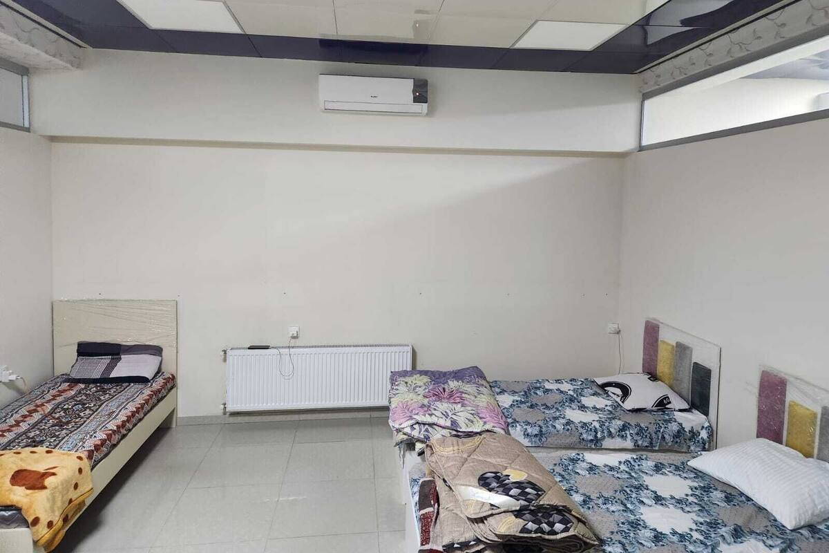 A room with two beds, a radiator, and an air conditioning unit on the wall.