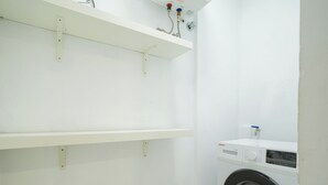 A laundry room with a washing machine, shelves, and plumbing.