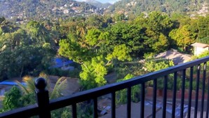 A balcony with a view of a densely vegetated hillside and scattered buildings. - Sesali Residences (Kandy)