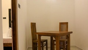 A small dining area with a wooden table and four chairs, a welcome mat, and a door leading to a bedroom. - Sesali Residences (Kandy)