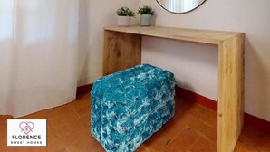 Habitación de esquina con una consola de madera, un espejo redondo, dos pequeñas macetas y un banco tapizado azul.