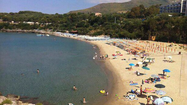 Ein Strand mit klarem Wasser, Sonnenschirmen und Menschen.