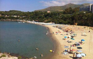 A beach with clear water, umbrellas, and people.