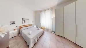 A bedroom with a bed, a nightstand, a wardrobe, and a floor lamp. - Charlotte apartment wheels (Firenze)