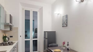 A compact kitchen with a refrigerator, a dining table with a vase of flowers, and a wall-mounted light fixture. - Charlotte apartment wheels (Firenze)