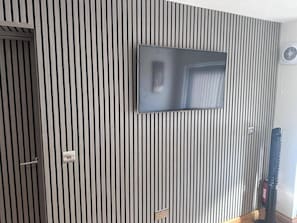 A room with a striped wall, a flat-screen TV mounted on the wall, a door, and a fire extinguisher. - Studio in Penrith - Sleeps 2 - Parking (Penrith)