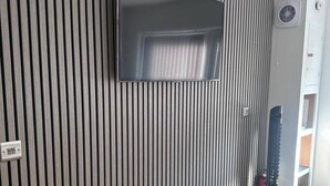 Ein Zimmer mit einem wandmontierten Flachbildfernseher, einer Lüftung und einer Tür mit Fenster.