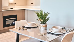 A modern kitchen with white cabinetry, a dining table set with plates, bowls, and cutlery, and a potted fern on the table. - Cozy Studio in Bracknell With Free Parking (Bracknell)