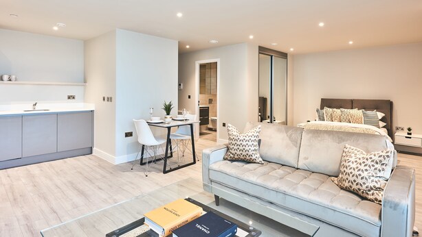 A modern apartment with a kitchenette, dining area, and a bedroom with a large bed and patterned pillows. - Cozy Studio in Bracknell With Free Parking (Bracknell)