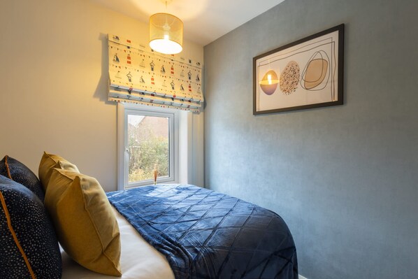 A bedroom with a bed, a window, a hanging light fixture, and a framed artwork on the wall. - Host Stay The Braes (Redcar)