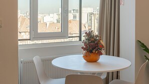 A room with a round table, two chairs, a window with a view of buildings, and a plant on the windowsill. - Charming 2BR Apartment - Steps to Romanian Athenaeum (Bucharest)