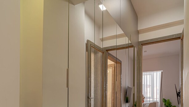 A hallway with a mirrored wall, wooden flooring, and a dining area in the background. - Charming 2BR Apartment - Steps to Romanian Athenaeum (Bucharest)