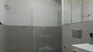 Une salle de bain moderne dotée d’une douche à parois de verre, de toilettes et d’un meuble-lavabo avec un miroir.