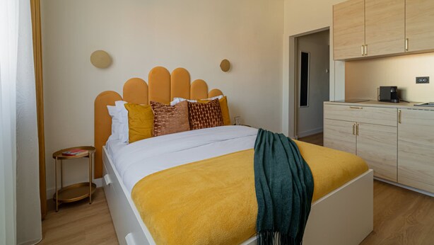 Une chambre à coucher moderne avec un lit, une table de chevet et une vue sur la cuisine.