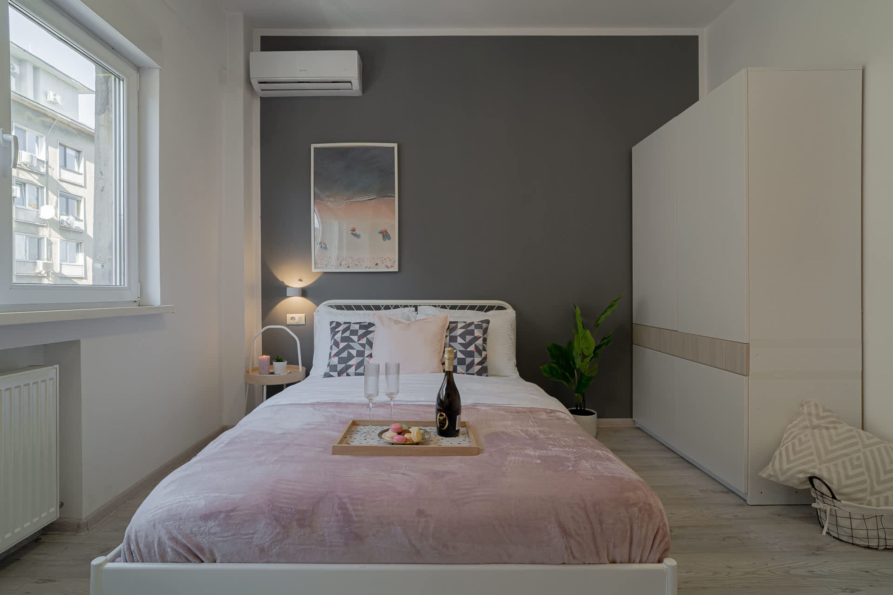 Un dormitorio con cama, mesita de noche, lámpara, aire acondicionado, una obra de arte y ventana.