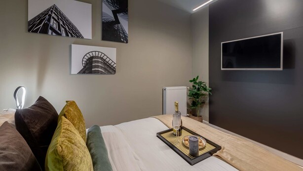A modern hotel room with a bed, a flat-screen TV, and artwork on the walls.