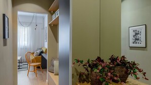 A hallway with a wooden floor, a desk with a basket of plants, and a chair.