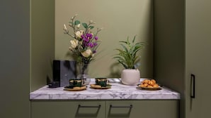 A kitchen counter with a marble top, a coffee machine, a vase with flowers, a potted plant, and a plate of pastries. - Serene 1BR Apartment in University Square (Bucharest)