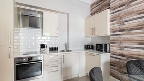 A modern kitchen with white cabinets, stainless steel appliances, and a wooden accent wall. - Host Stay Mayford Apartment (Durham)