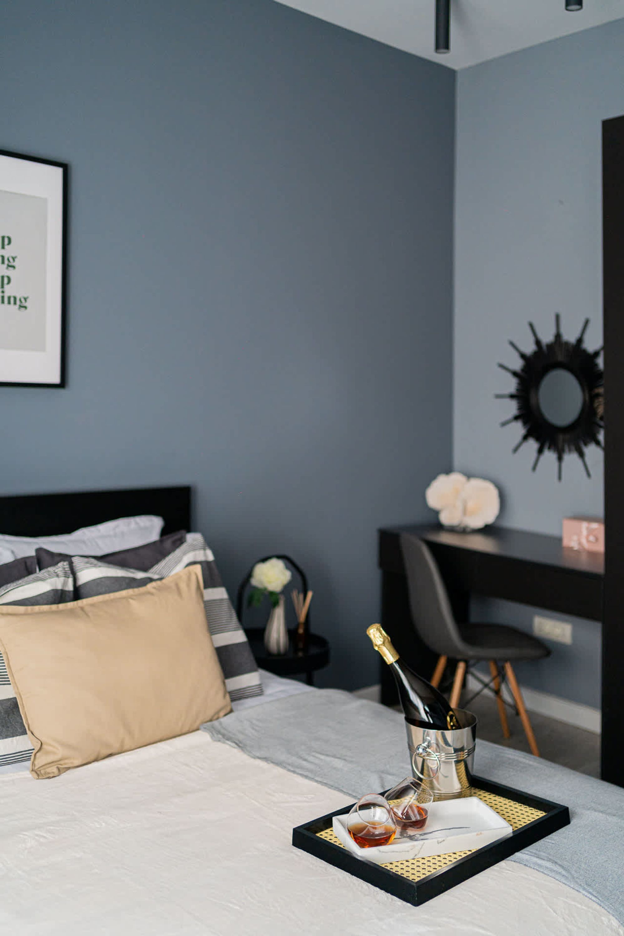 A neatly made bed with a tray of champagne, glasses, and a bottle. A desk with a chair and a decorative mirror are visible in the background.