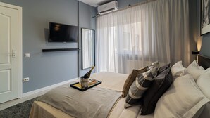 A hotel room with a bed, a television, an air conditioning unit, a window with sheer curtains, and a framed picture on the wall. - Chic Black White 2BR Retreat on Dambovitei (Bucharest)