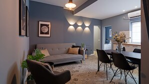 A modern living room with a grey sofa, black chairs, a dining table, and a hanging light fixture. - Chic Black White 2BR Retreat on Dambovitei (Bucharest)