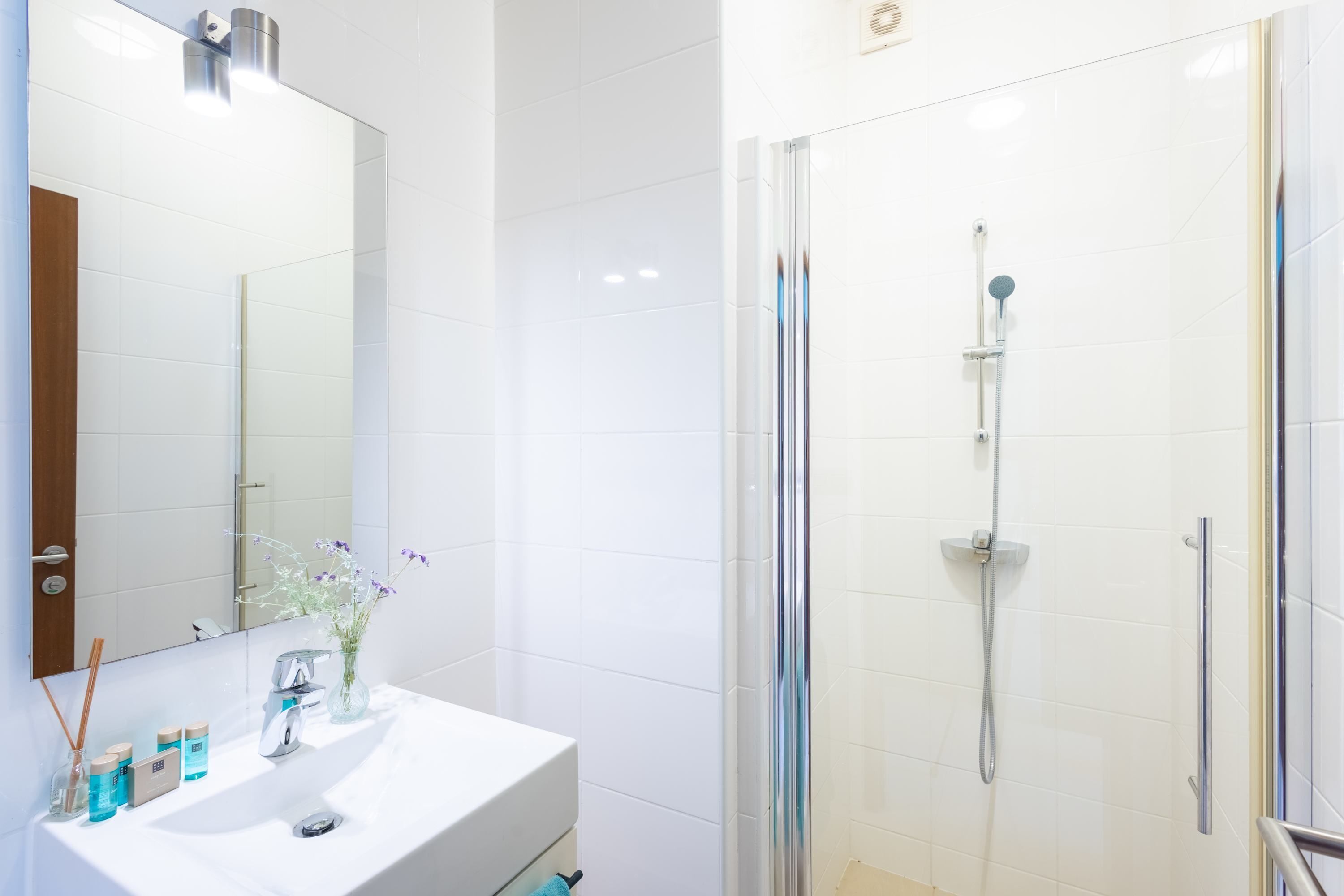 Un bany modern amb un lavabo blanc, un mirall i una dutxa amb envàs de vidre.